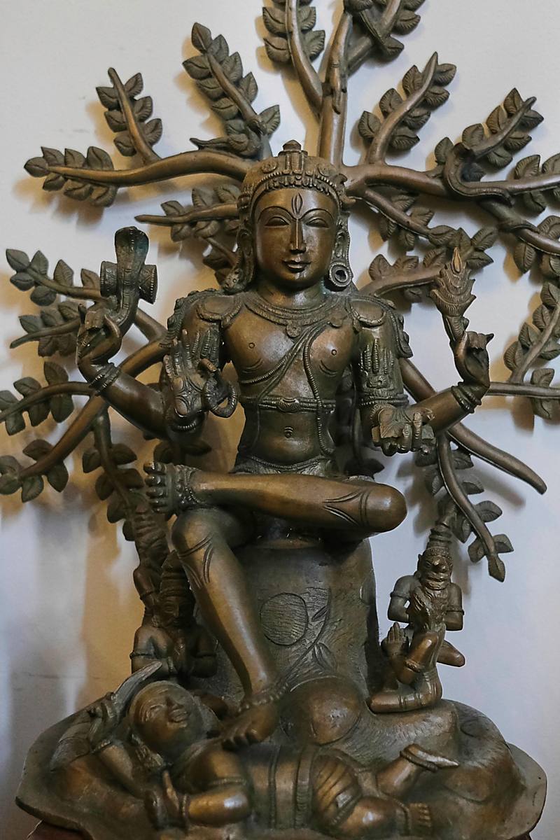 A bronze figure seated within a tree of leaves